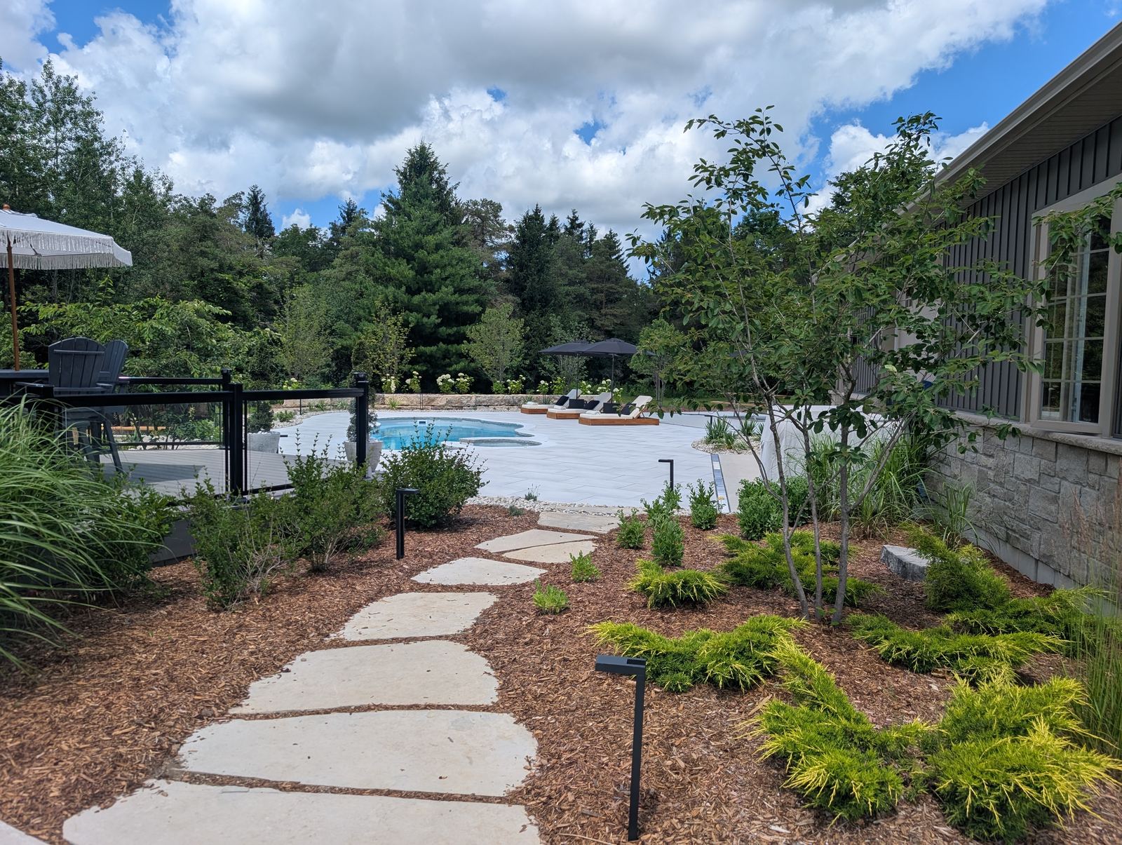 Garden path leading to a backyard pool beside a stone house